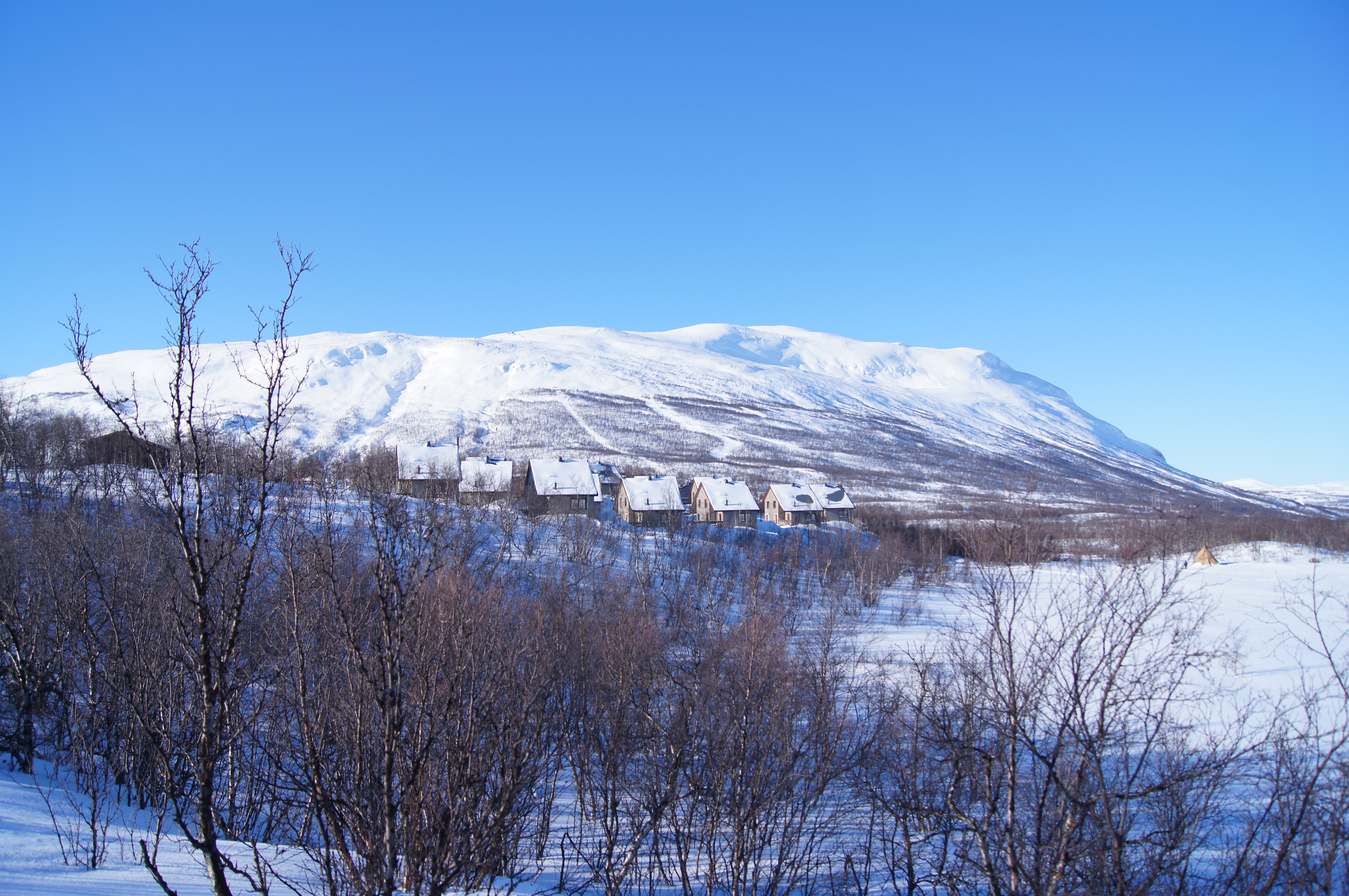 Snow-covered huts at STF Abisko Mountain Station with a mountain behind them.