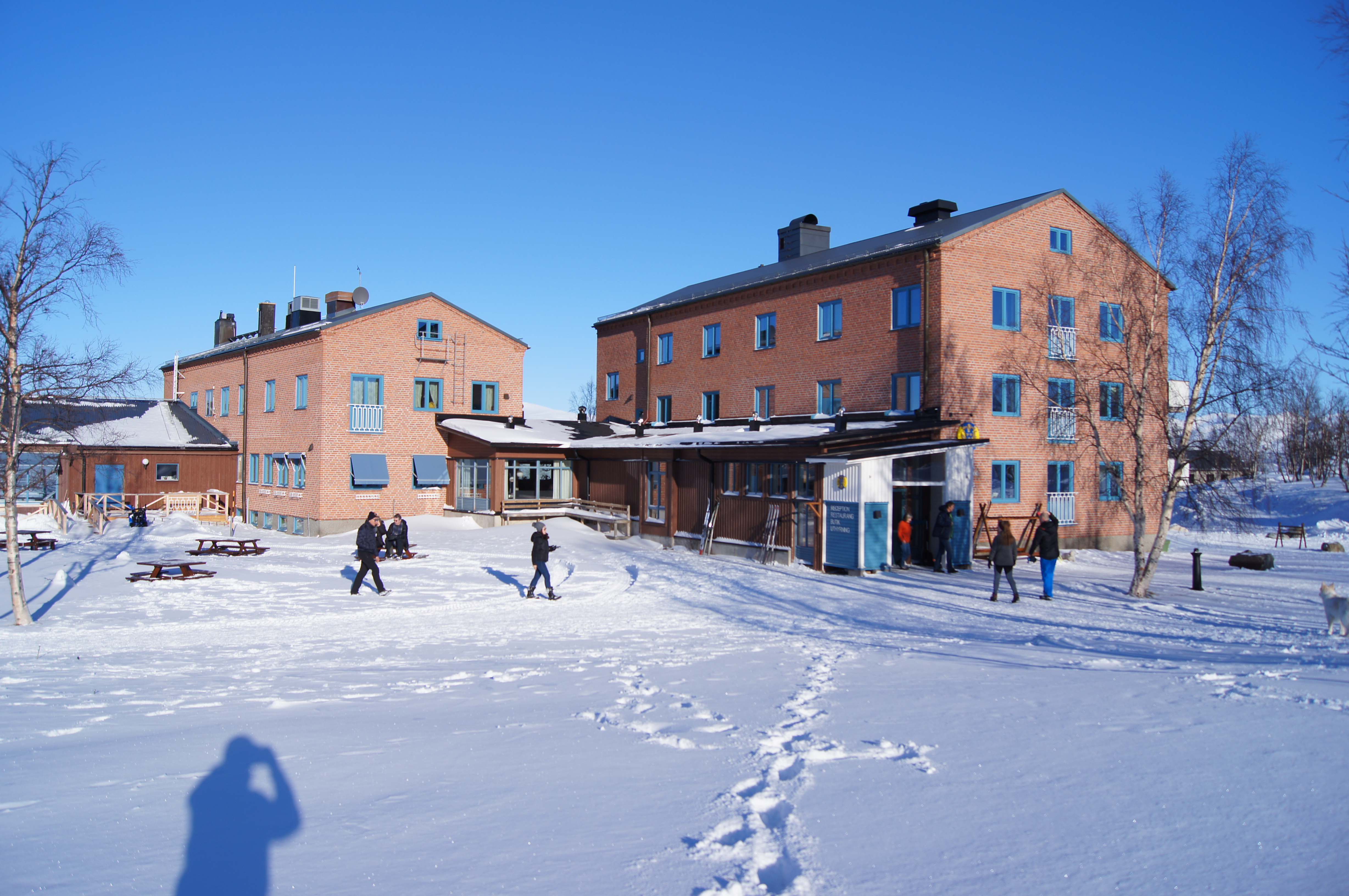 The brick main building at STF Abisko Mountain Station in snow, with visitors outside.