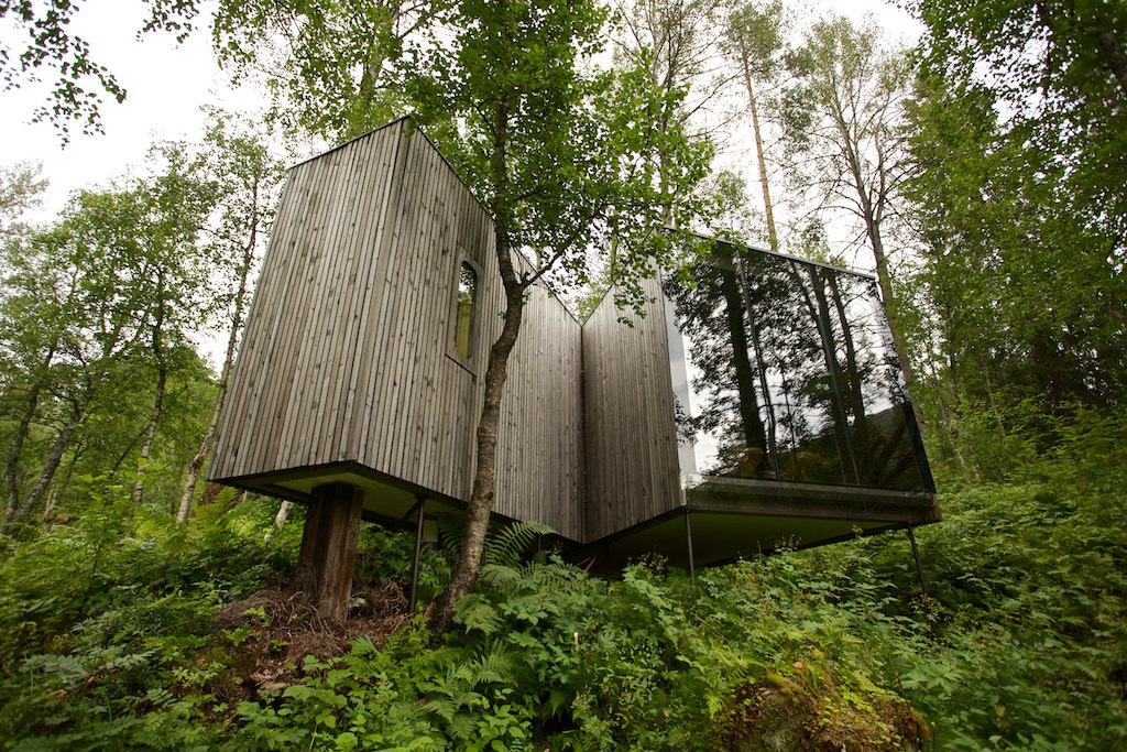 A timber-clad landscape room with a glass wall among the trees at Juvet.