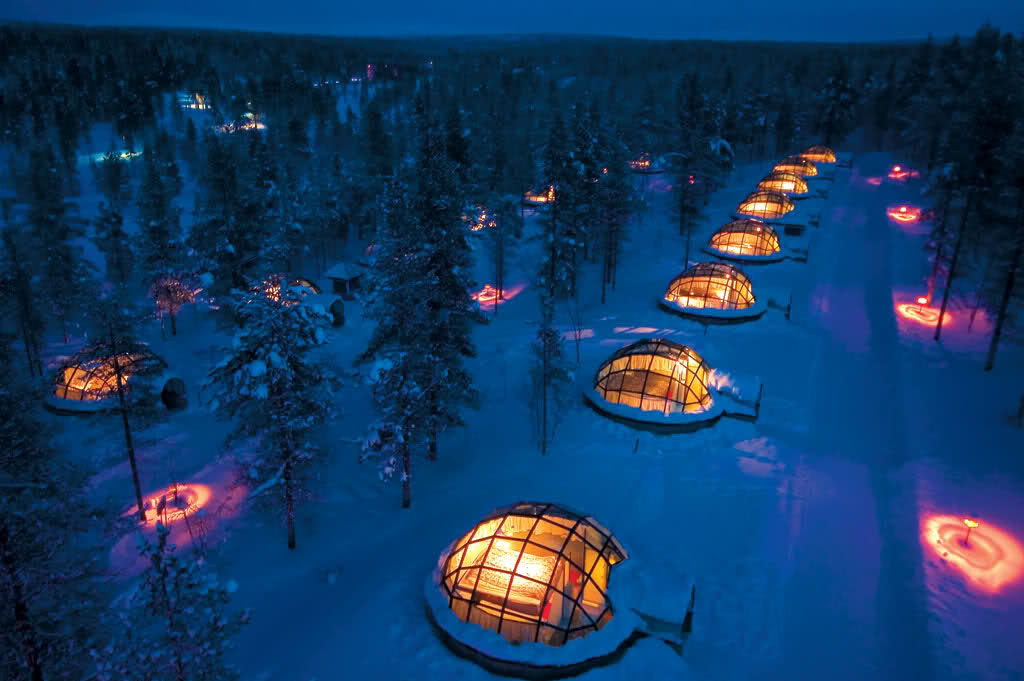Illuminated glass igloos among snow-covered pines at Kakslauttanen Arctic Resort.