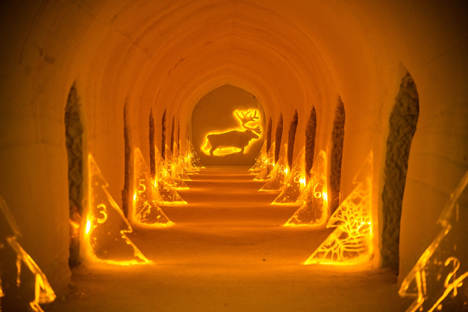 A golden-lit snow corridor with numbered room entrances inside Sorrisniva Igloo Hotel in Alta.