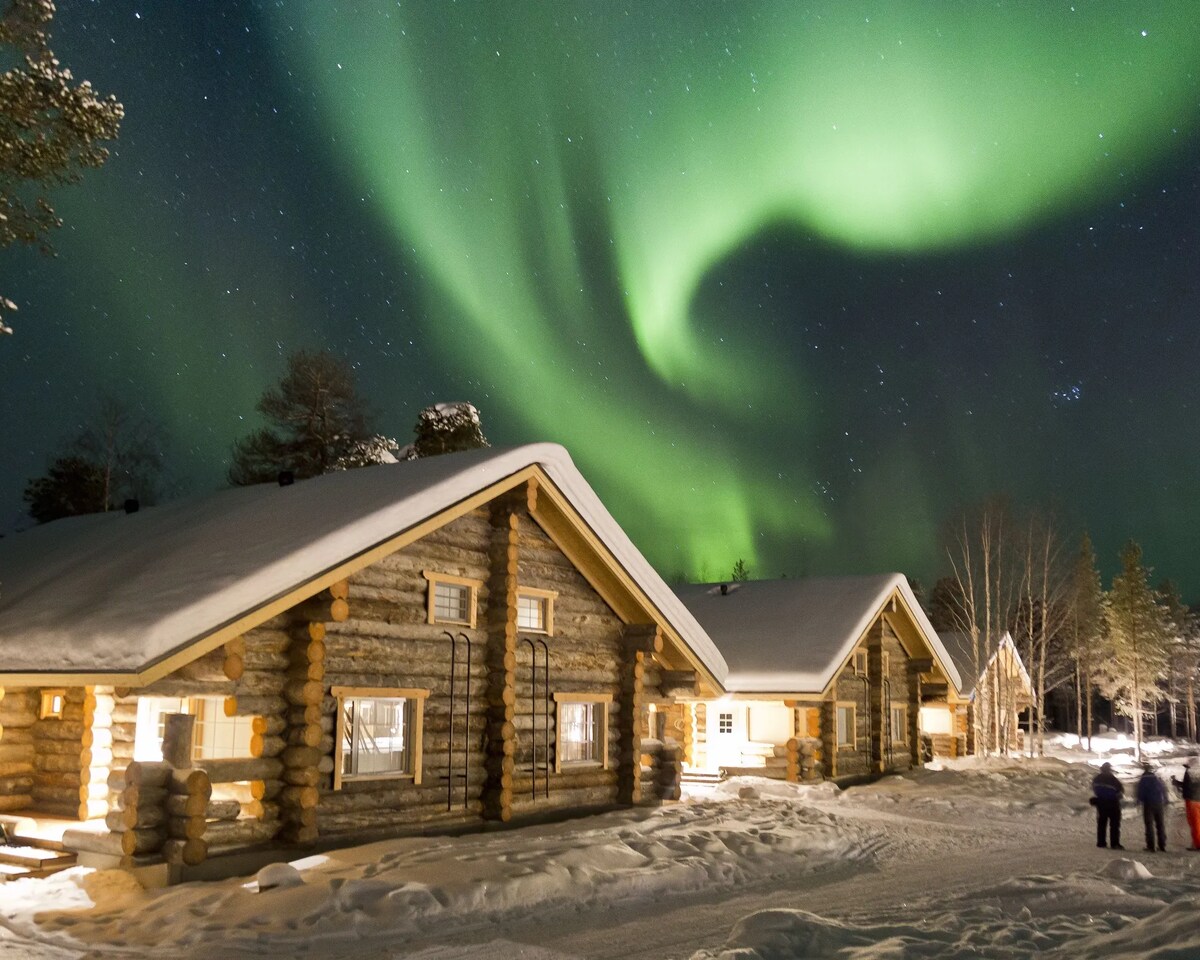 Snow-covered log cabins beneath northern lights at Wilderness Hotel Nellim
